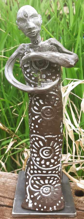 Keramikprodukt von Claudia Entner - Schmale Figur in schwarzem Ton, Körper mit gestempeltem Muster, das mit weißer Glasur ausgefüllt ist in ihren Händen hüttet sie eine Pflanze