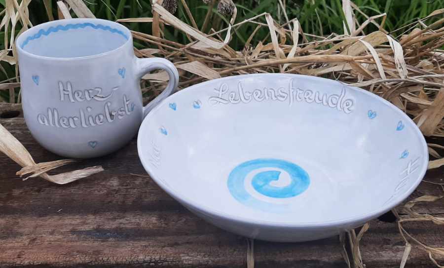 Keramikprodukte von Claudia Entner - eine Tasse und eine Schale, weiß glasiert, beides mit blauen Herzen, Tasse Aufschrift 'Herzallerliebst', Schale Aufschrift 'Lebensfreude' in der Mitte eine blaue Spirale